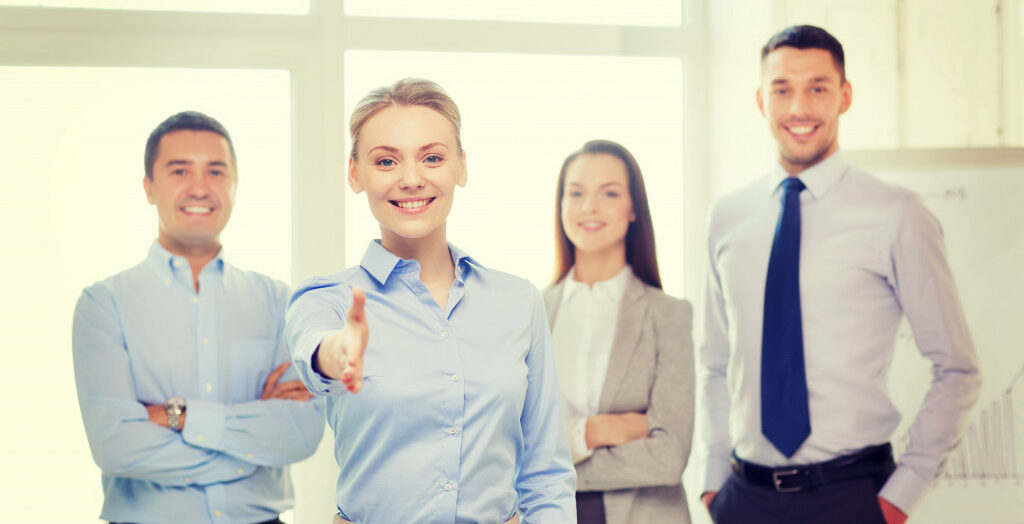 four smiling employees with one woman holding out her hand to invite