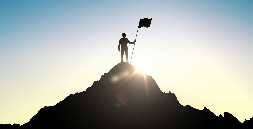 a silhouette of a man on top of a hill holding a flag as the sun shines on the background