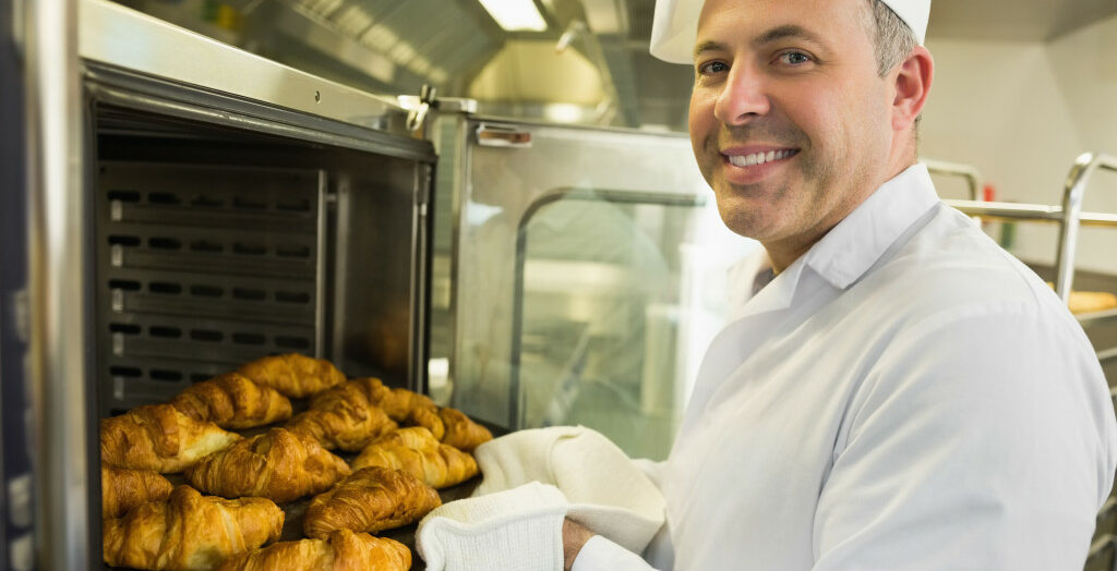 a smiling baker getting pastry from the oven