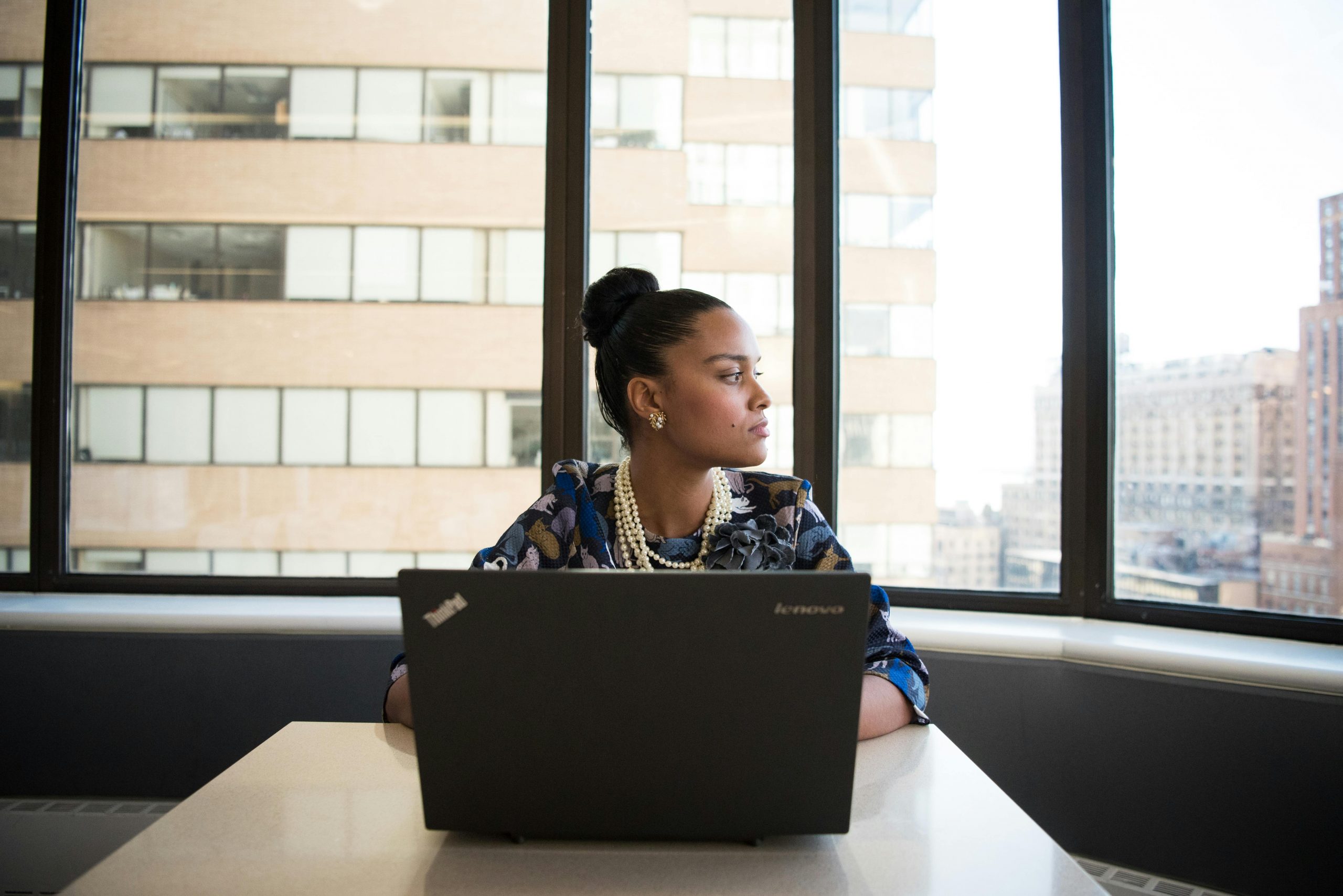 employee working on a laptop while gazing thoughtfully out a large office window