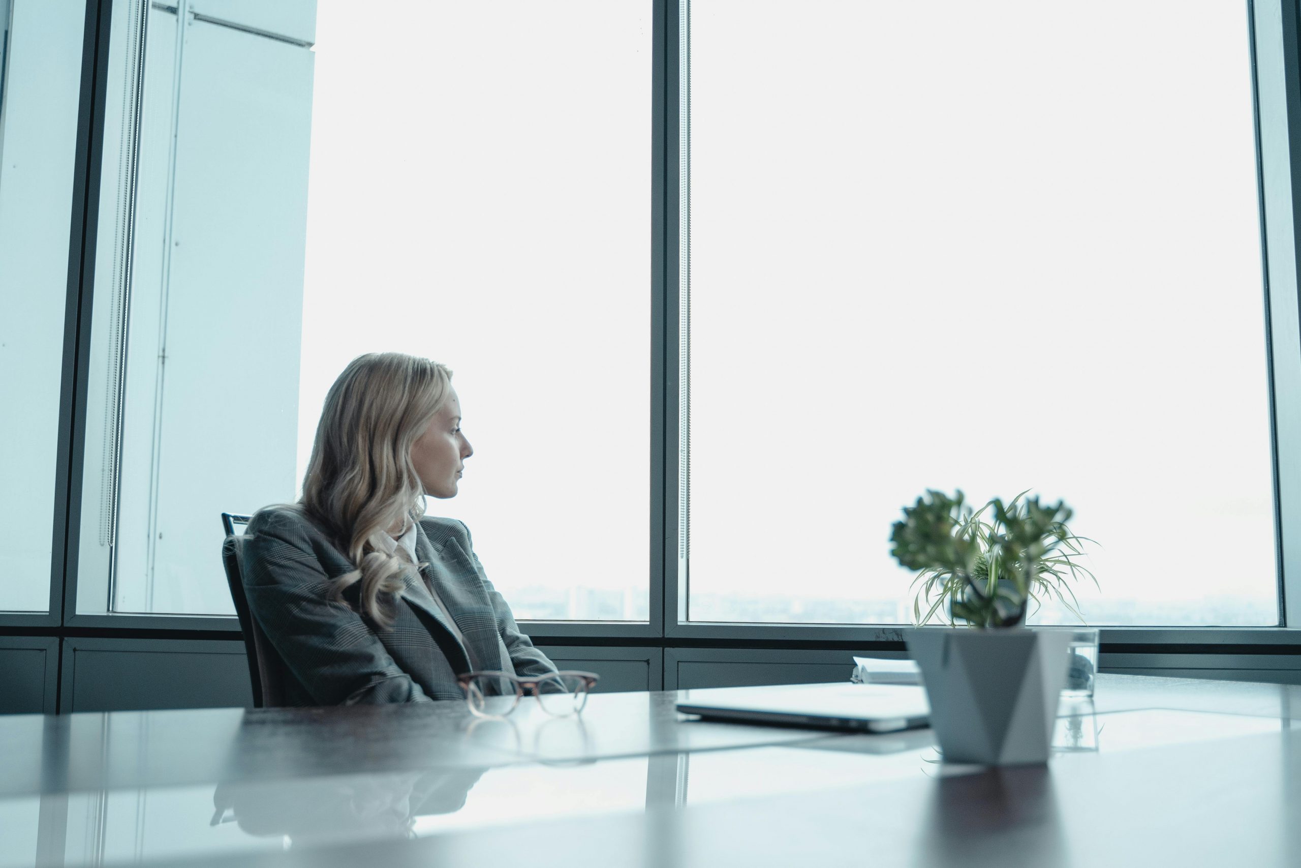 professionally dressed woman thoughtfully looking out a large office window